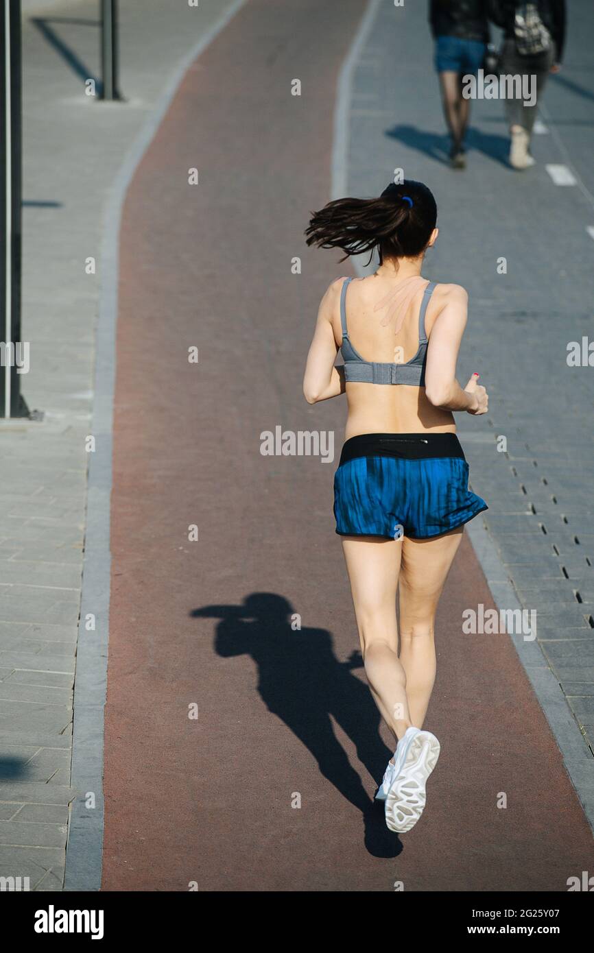 Tall athletic woman running away on the new track outdoors next to a  walkway. On a