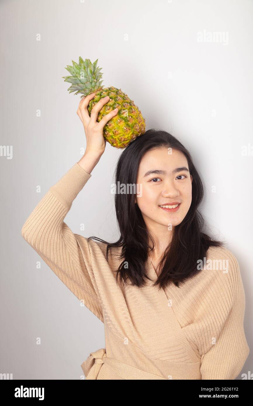 Young Asian Woman holding a pineapple on her head Stock Photo