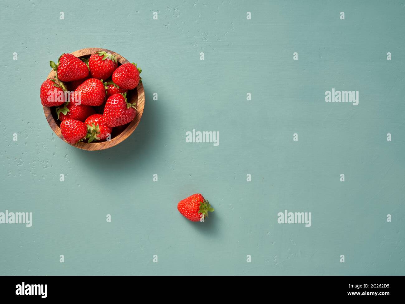 Fresh strawberry on a blue background. Top view of strawberries with leaves in wooden bowl. Stock Photo
