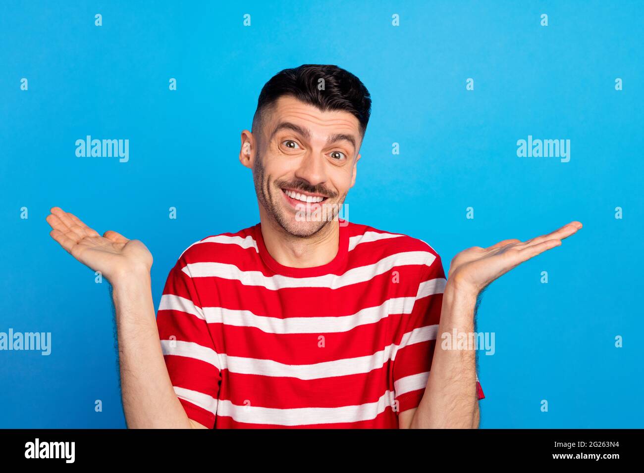 Photo of funny puzzled young man wear striped tshirt rising arms