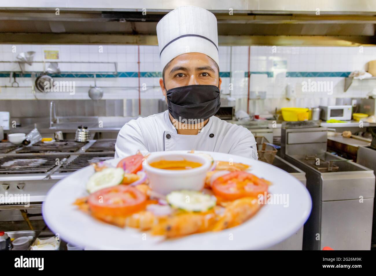 Portrait of Mexican Chef presenting plate in kitchen Stock Photo