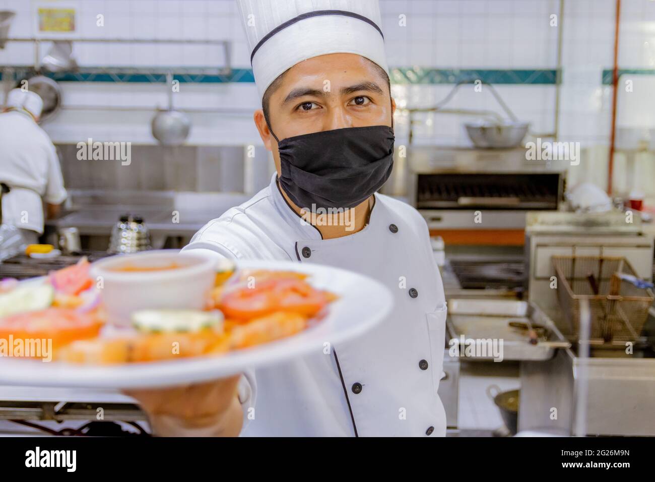 Portrait of Mexican Chef presenting plate in kitchen Stock Photo