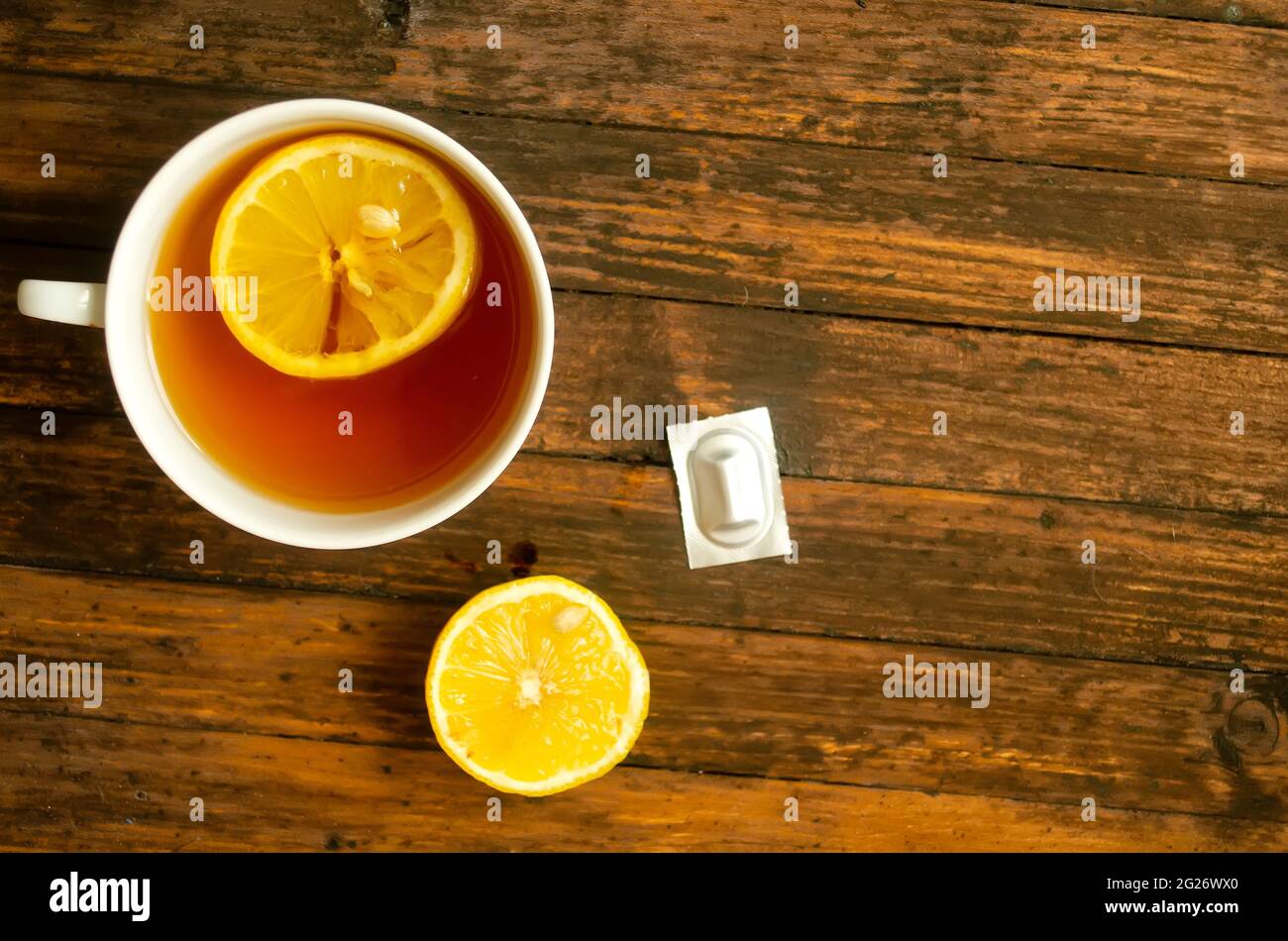 Top view, a cup of tea with lemon, a half of lemon and one pill on wooden background, copyspace. Stock Photo