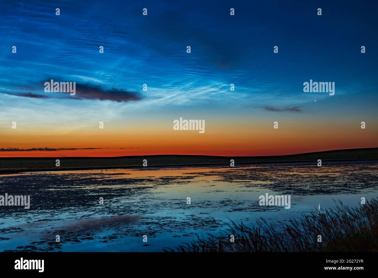 Bright noctilucent clouds in the dawn sky over a prairie pond in southern Alberta, Canada. Stock Photo