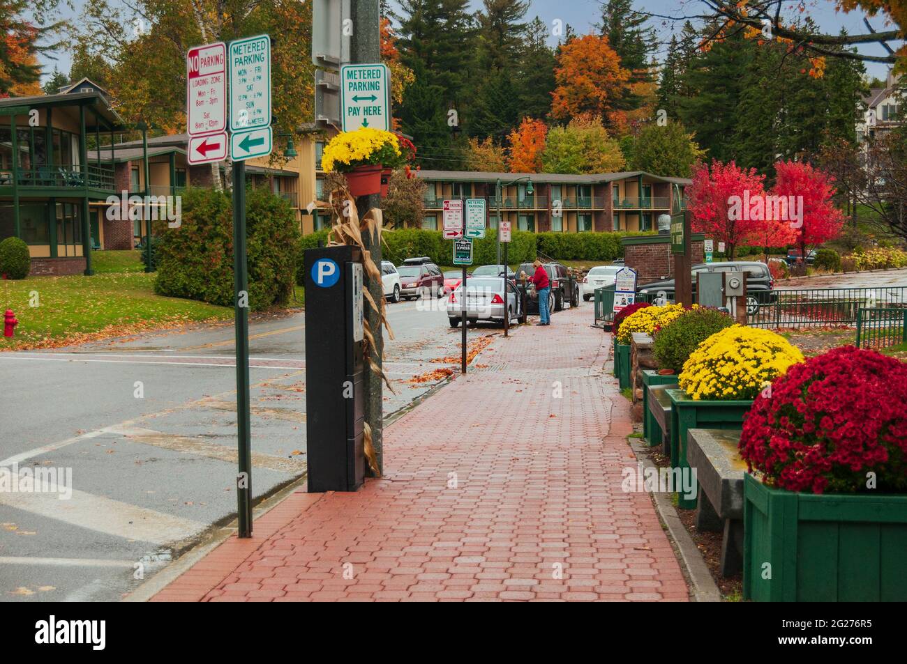 A woman plugs a parking meter on a colorful street with flower boxes in Lake Placid, New York, USA. Stock Photo