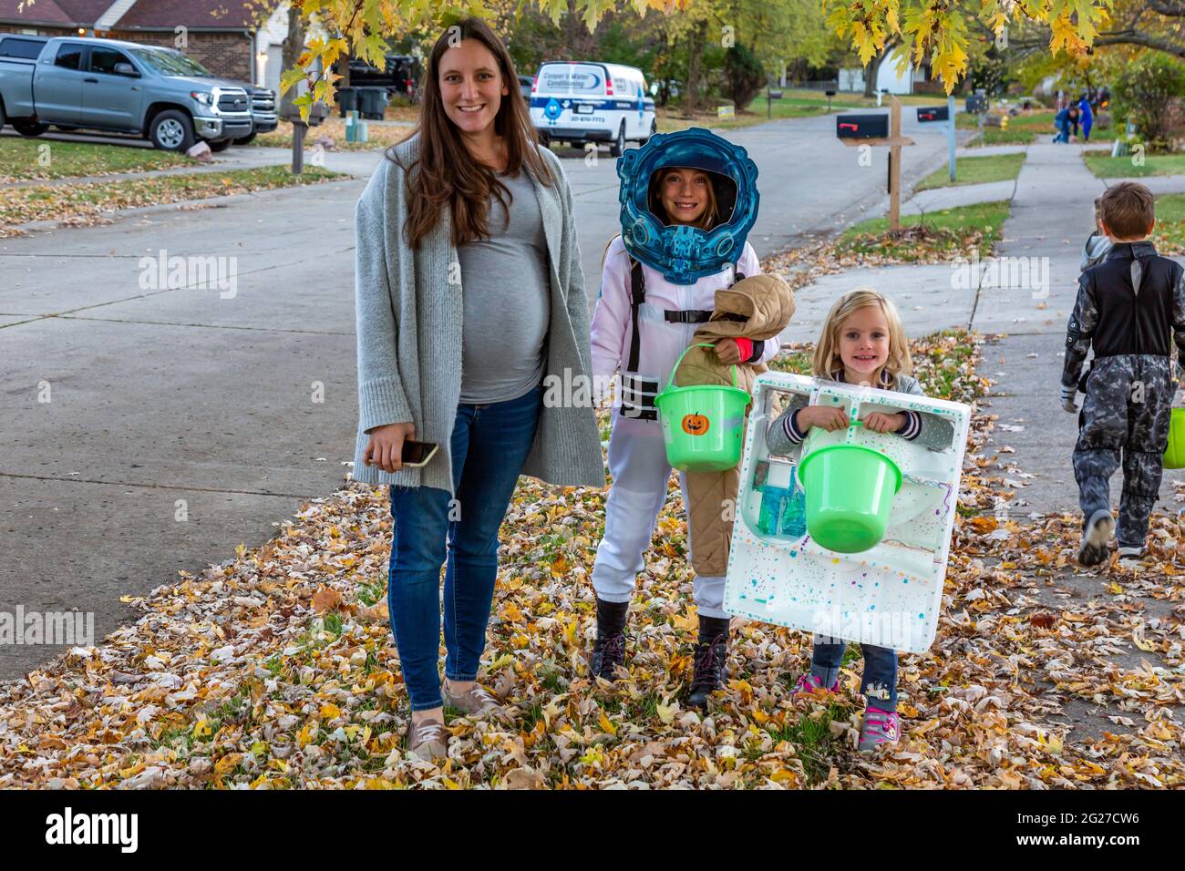 A pregnant woman and accompanies her children as they celebrate Halloween by trick or treating in their Lawrence, Indiana neighborhood. Stock Photo