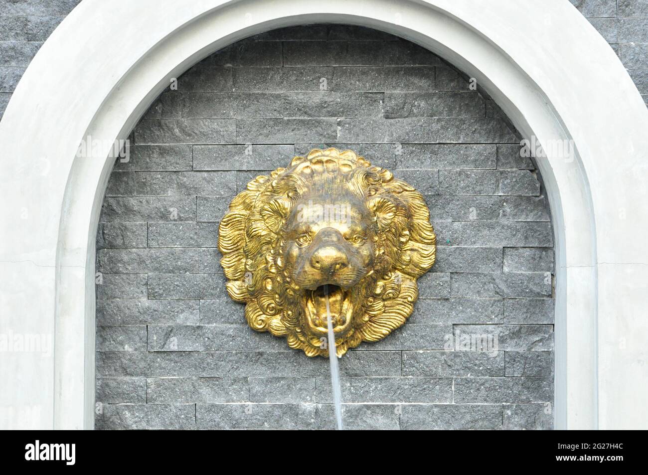 Golden lion head sculpture on stone wall spouting water Stock Photo