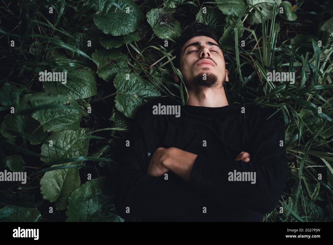 Young man in the forest lying on wet grass and daydreaming while thinking Stock Photo
