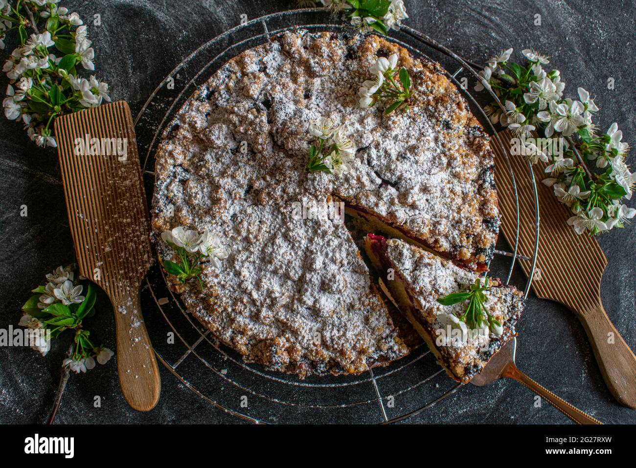 Fruitcake isolated on dark background. Cherry crumble cake on a cooling rack with cherry blossoms on a dark table Stock Photo