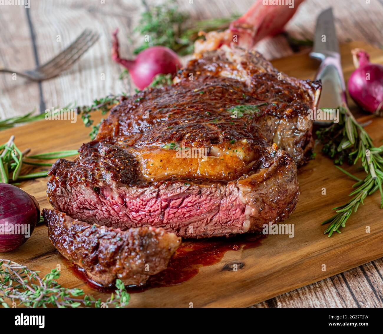 fresh grilled dry aged and irish tomahawk rib eye steak served on a rustic and wooden cutting board with herbs and steak knife Stock Photo
