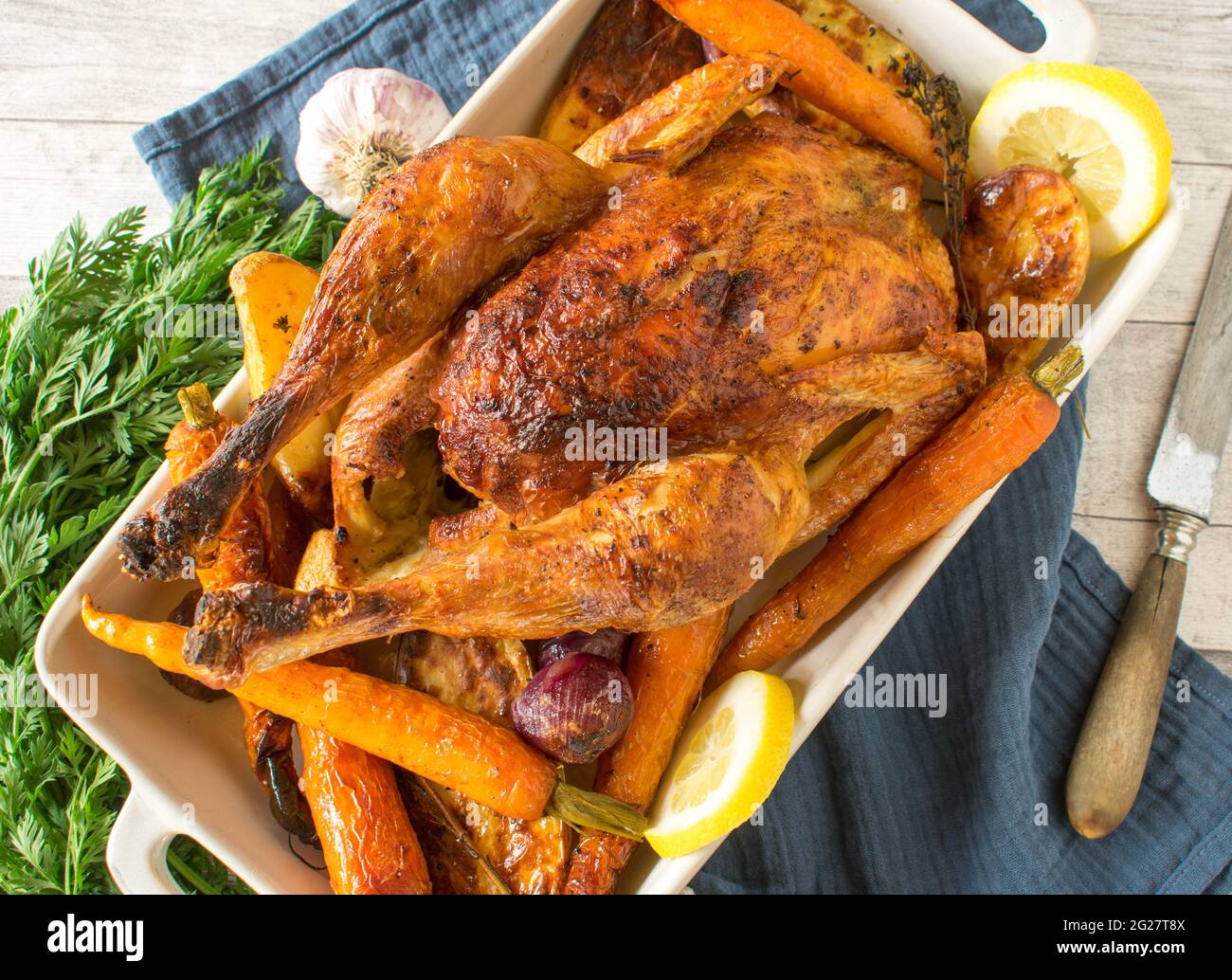 Roast chicken with oven vegetables served in a baking dish on rustic and wooden table background. Closeup and isolated view Stock Photo