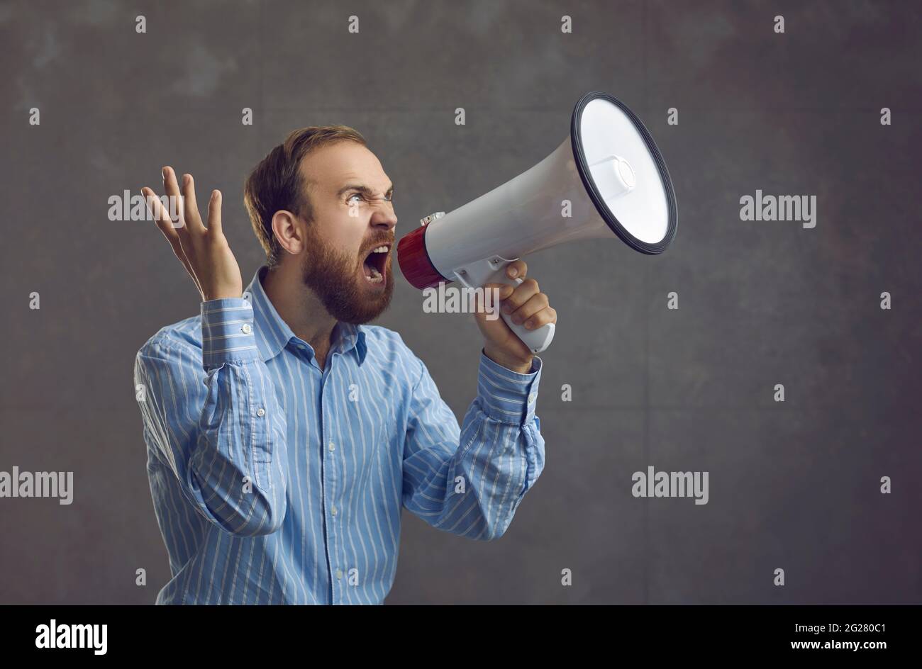 Excited young businessman in a blue shirt holding a megaphone and shouting like crazy Stock Photo