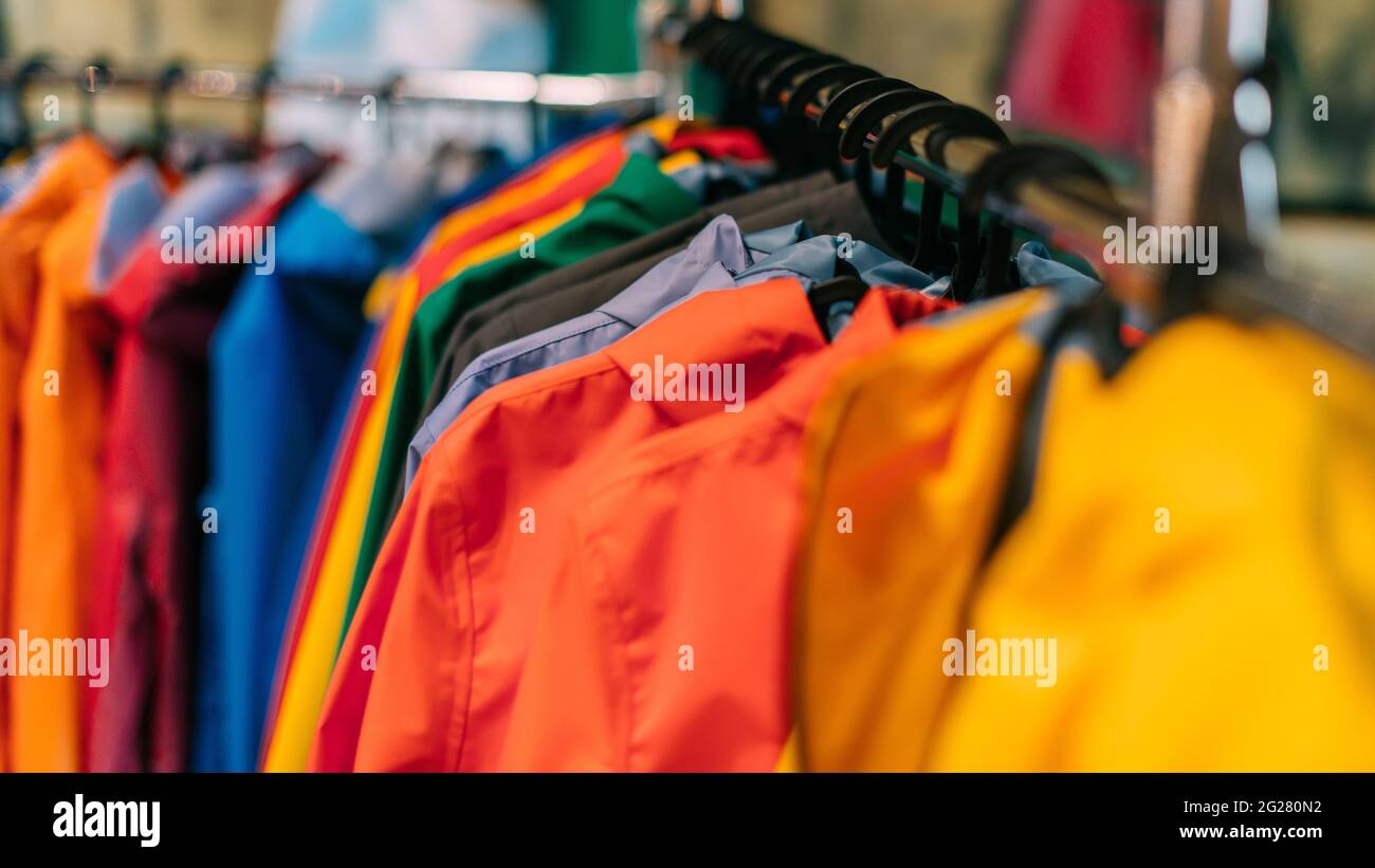 Multicolored rain jackets hang on hangers in the store. Stock Photo