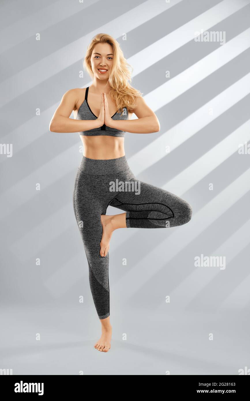 Front view of smiling attractive blonde young woman standing in pose yoga  in trendy sportswear on grey background. Concept of meditation and yoga for  improve body Stock Photo - Alamy