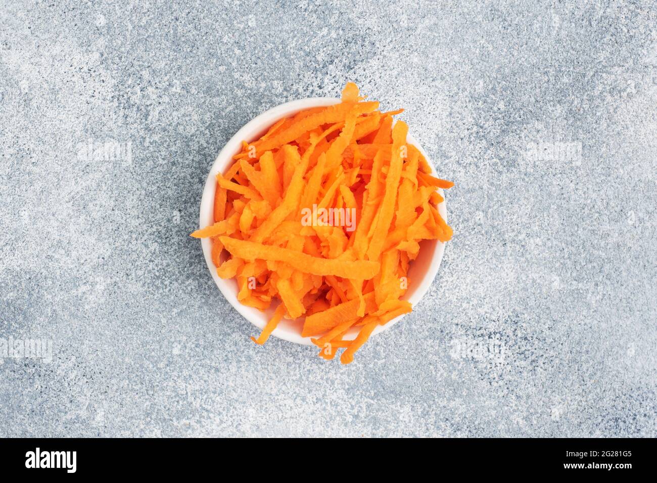 Grated carrots in a white plate. Raw vegetables, ingredients for roasting. gray background, copy space, top view Stock Photo