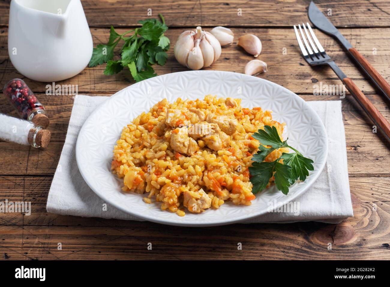 Delicious Asian pilaf, stewed rice with vegetables and chicken on a plate. Wooden rustic background Stock Photo
