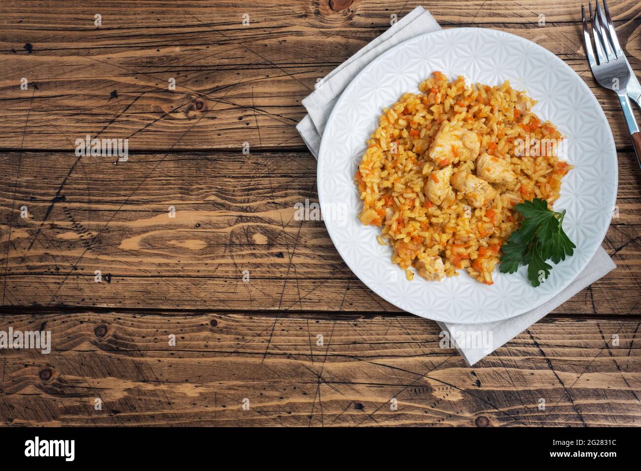 Delicious Asian pilaf, stewed rice with vegetables and chicken on a plate. Wooden rustic background copy space. Stock Photo