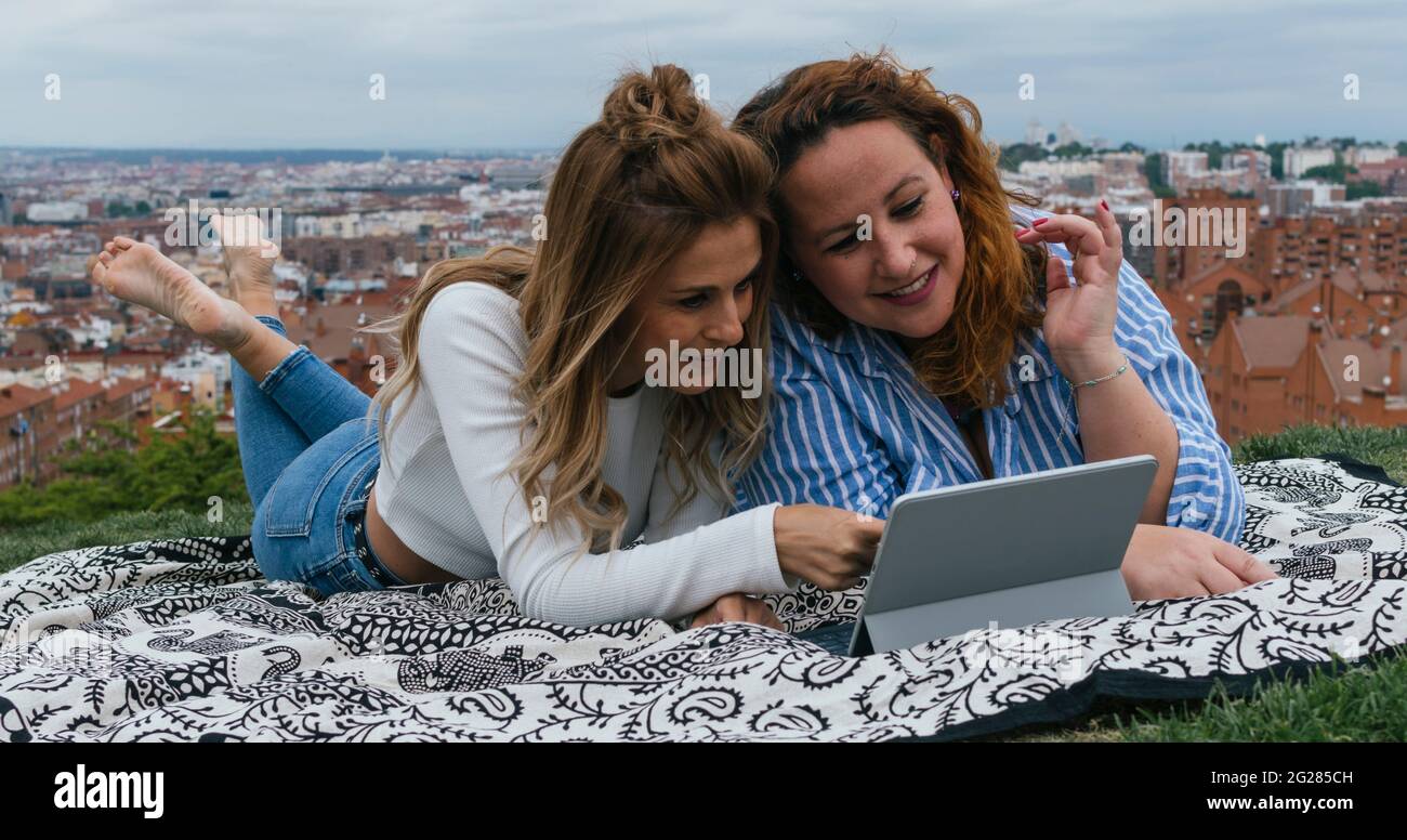 Young girls lying on a lawn looking at a tablet Stock Photo - Alamy