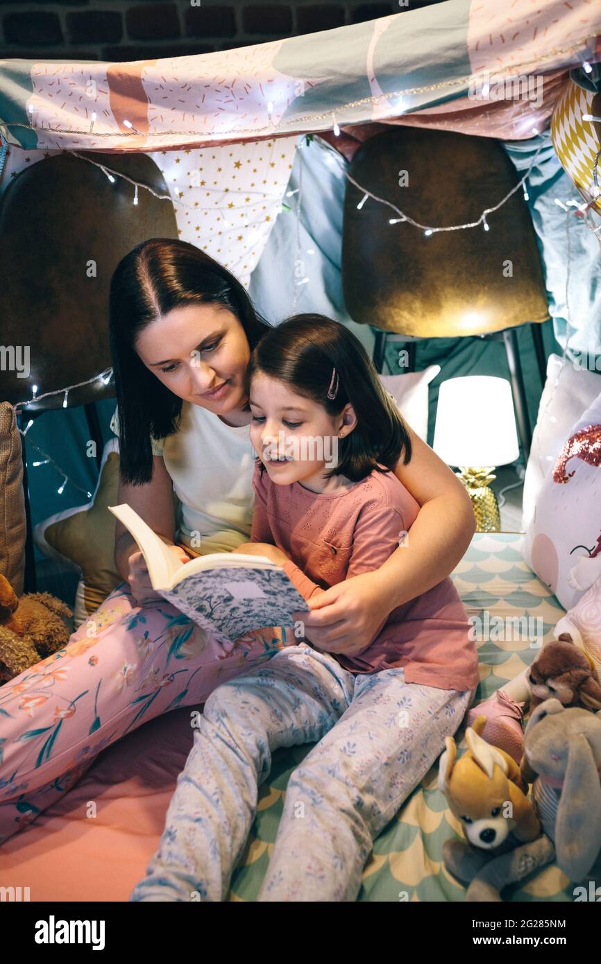 Girl reading with her mother in a makeshift tent at home Stock Photo