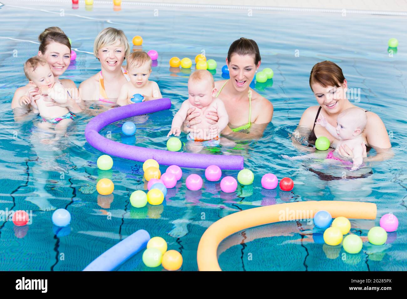 Moms and their newborns playing together with balls and pool noodles at