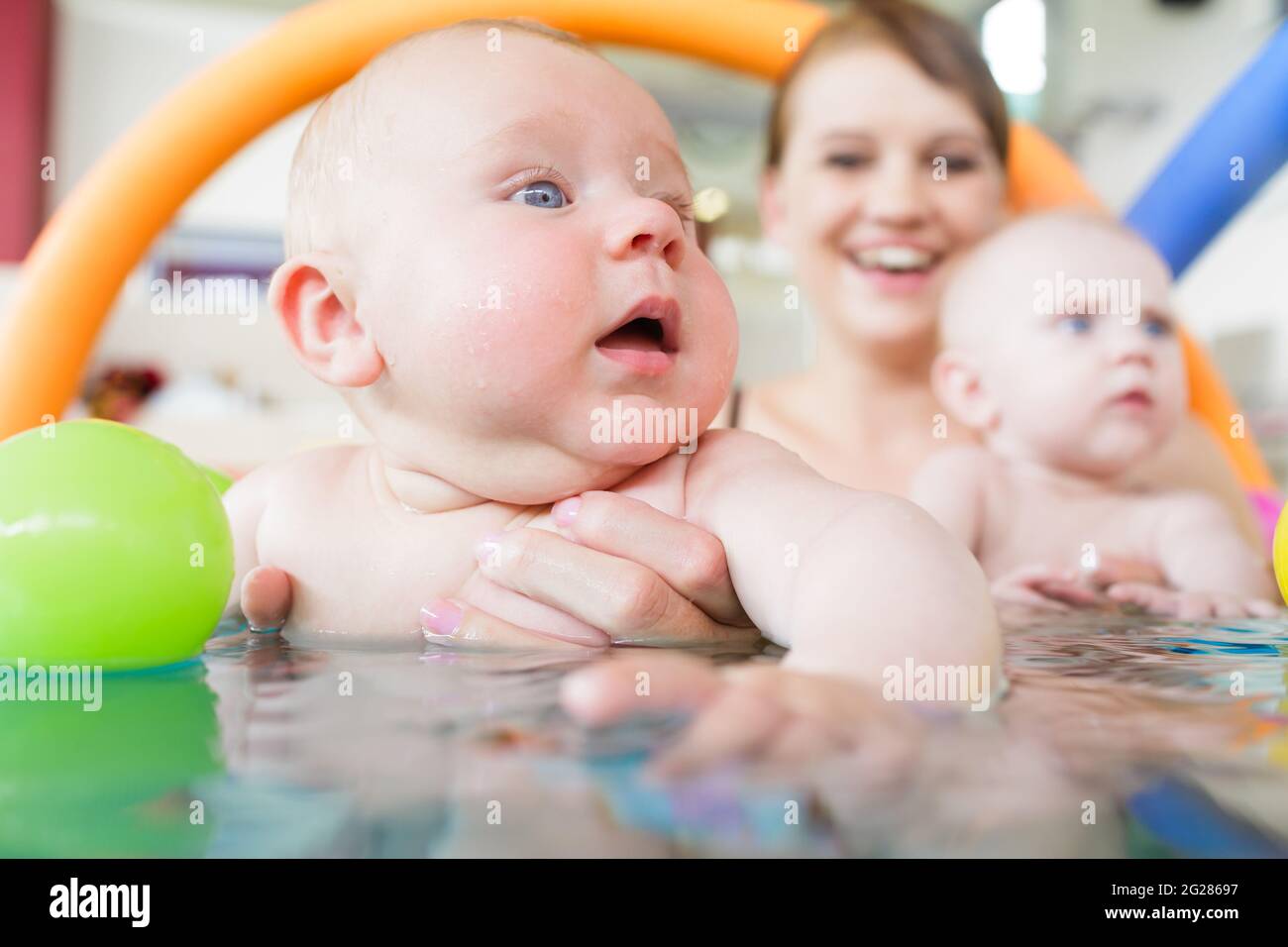 Newborn baby in pool at infant swimming lesson reaching for water ball