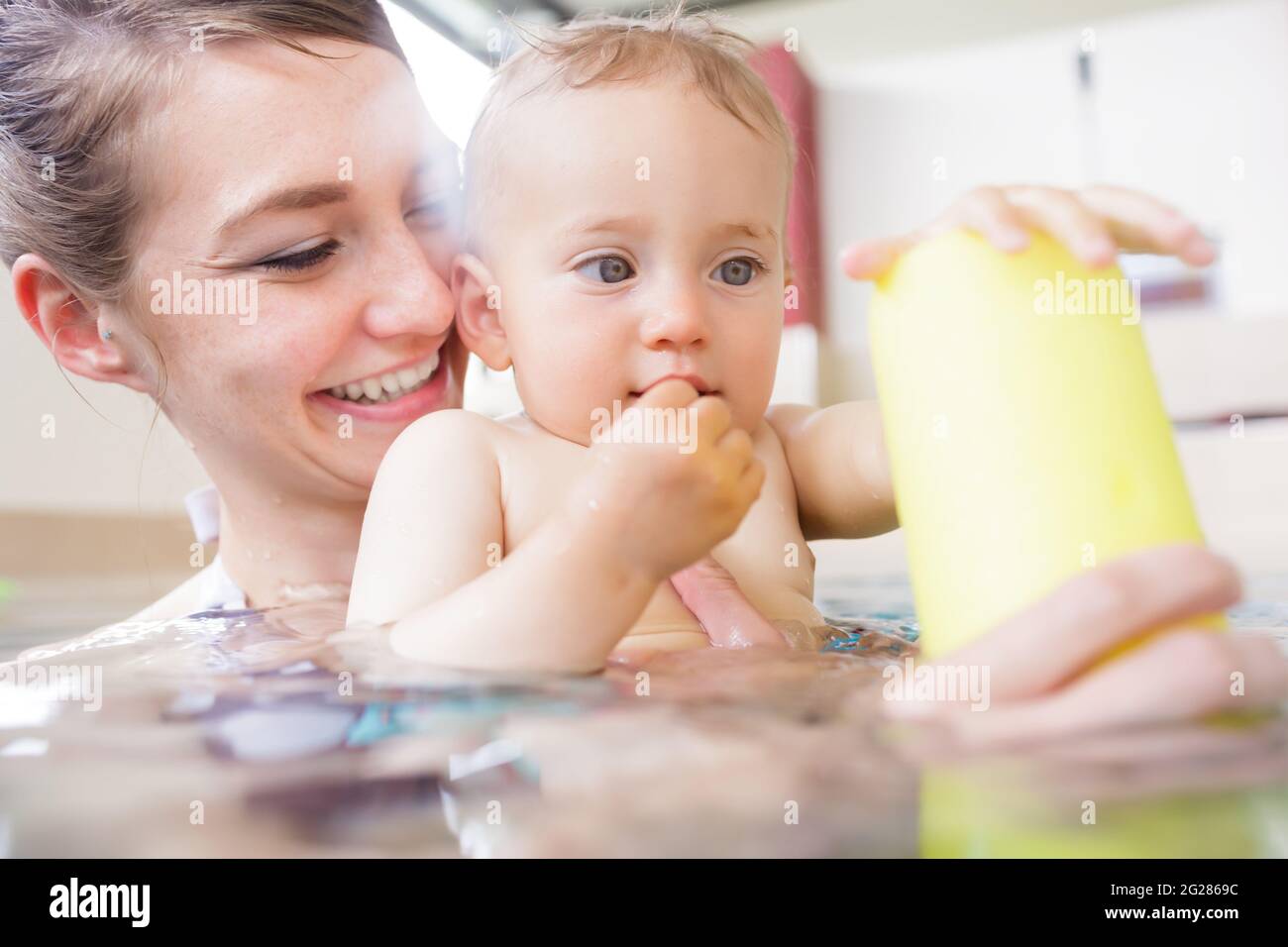 Newborn baby in pool at infant swimming lesson reaching for water ball