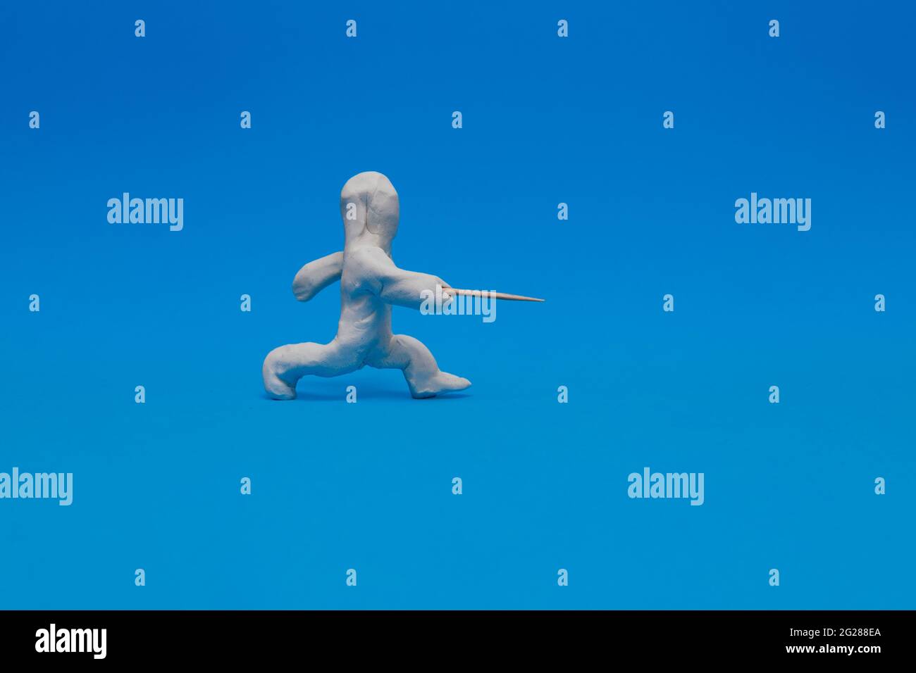 White plasticine dummy practicing fencing on a blue background. The dummy is making a thrust with his foil. Stock Photo