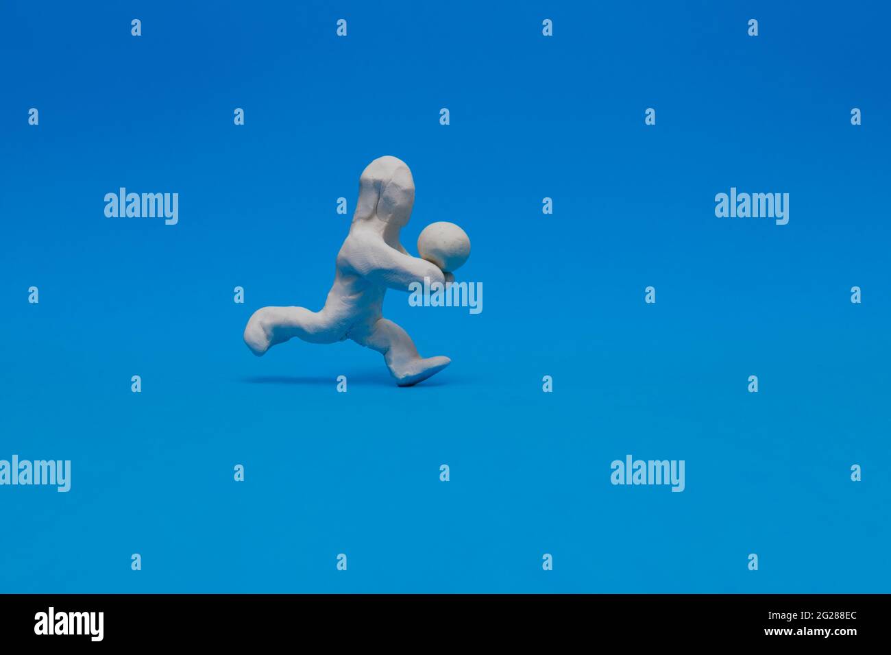 White plasticine doll practicing volleyball on a blue background. The doll is receiving the ball hitting it with his forearms. Stock Photo