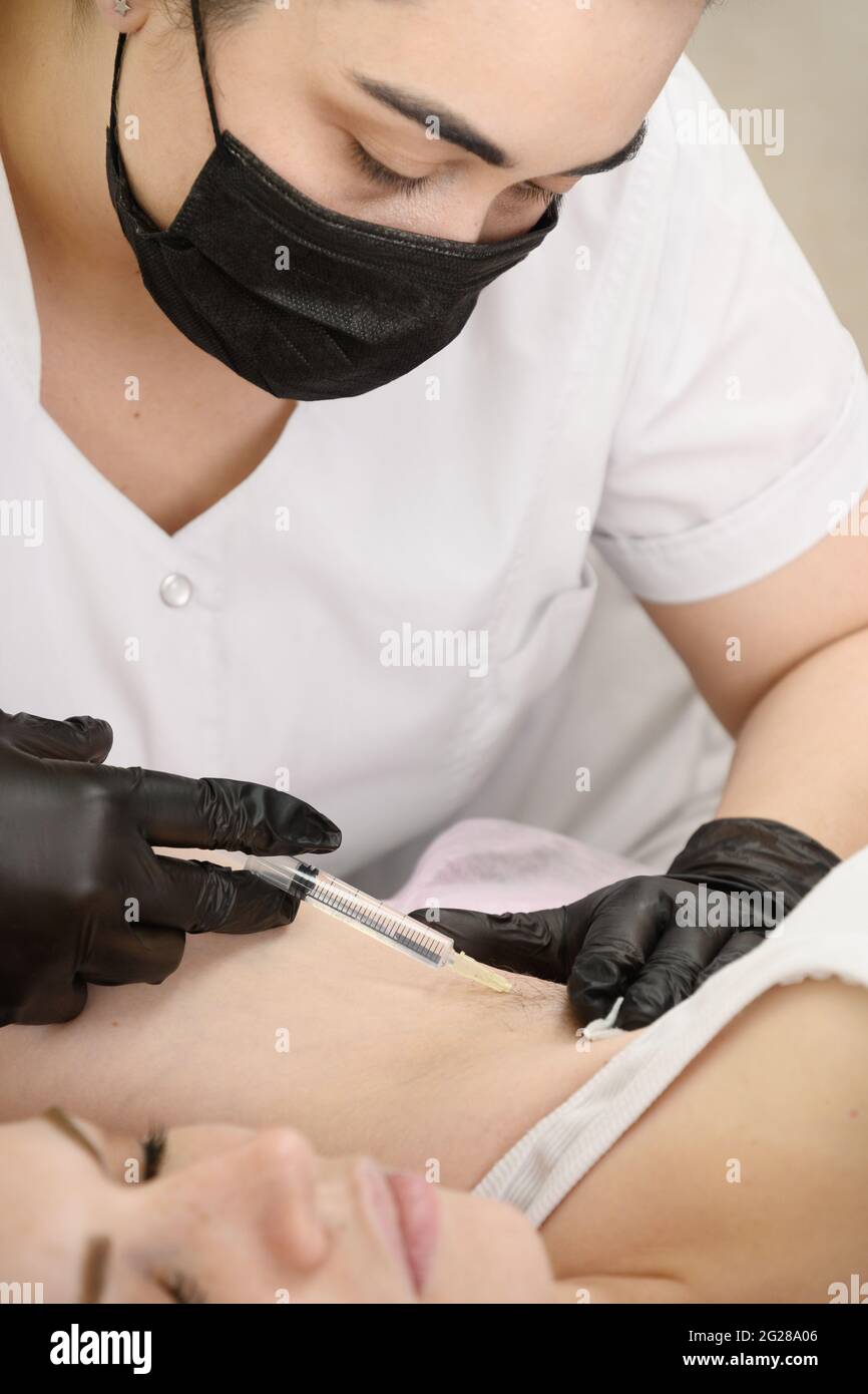 Doctor electrologist gives an injection of anesthesia into the armpit before the electrolysis procedure Stock Photo