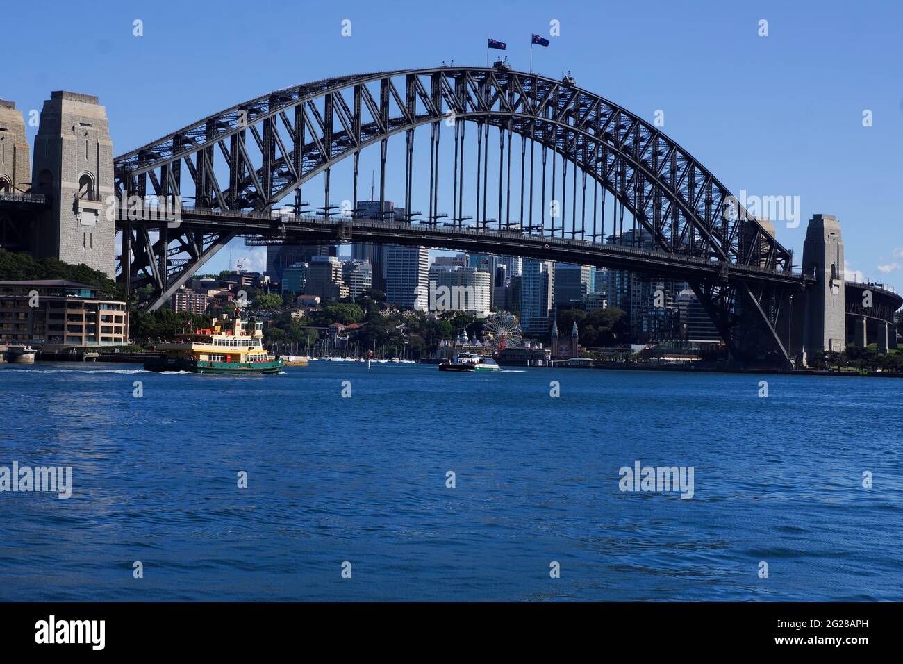Iconic Sydney harbour bridge with a ferry passing underneath against a blue sky with blue water and copy space. Stock Photo