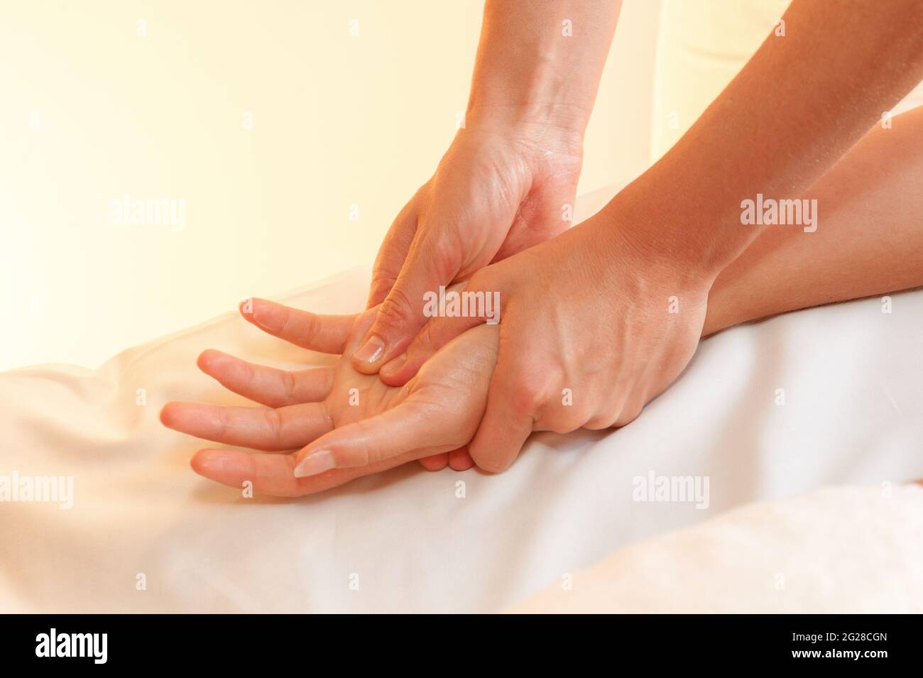Hands of female masseuse massaging woman hand palm in beauty spa salon. warm light Stock Photo