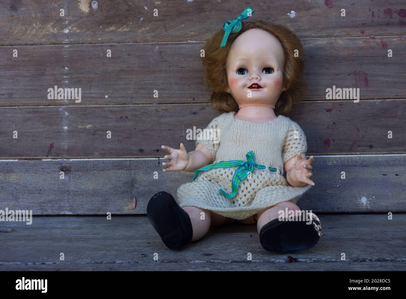 Scary creepy old vintage doll with staring eyes and blond hair in a knitted dress against a rustic background with copy space. Stock Photo