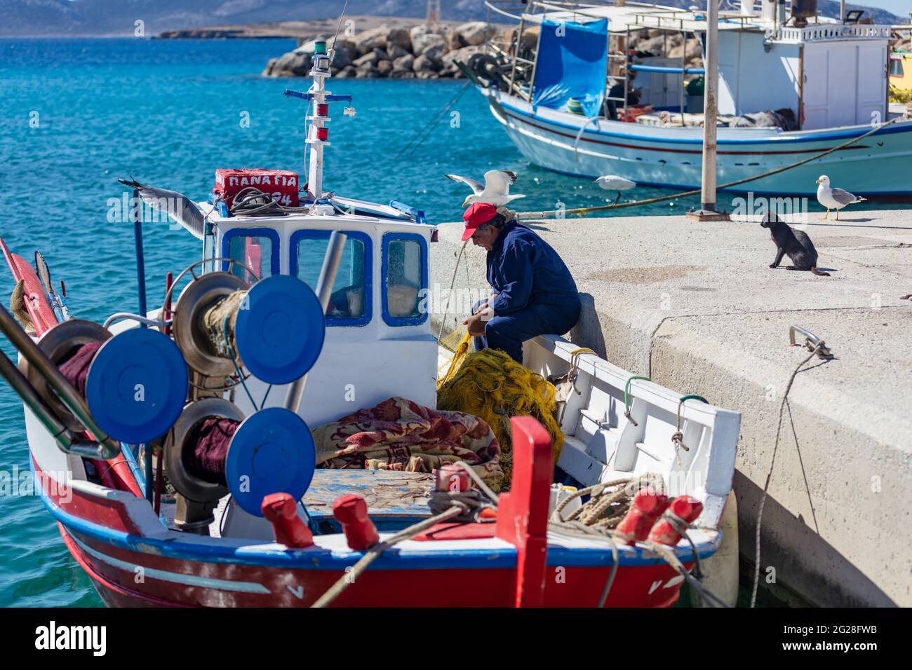 Greece. Koufonisi island, Cyclades, May 23, 2021. Afetr fishing scene at harbour dock. Fisherman working with the nets on a moored boat, seagulls look Stock Photo