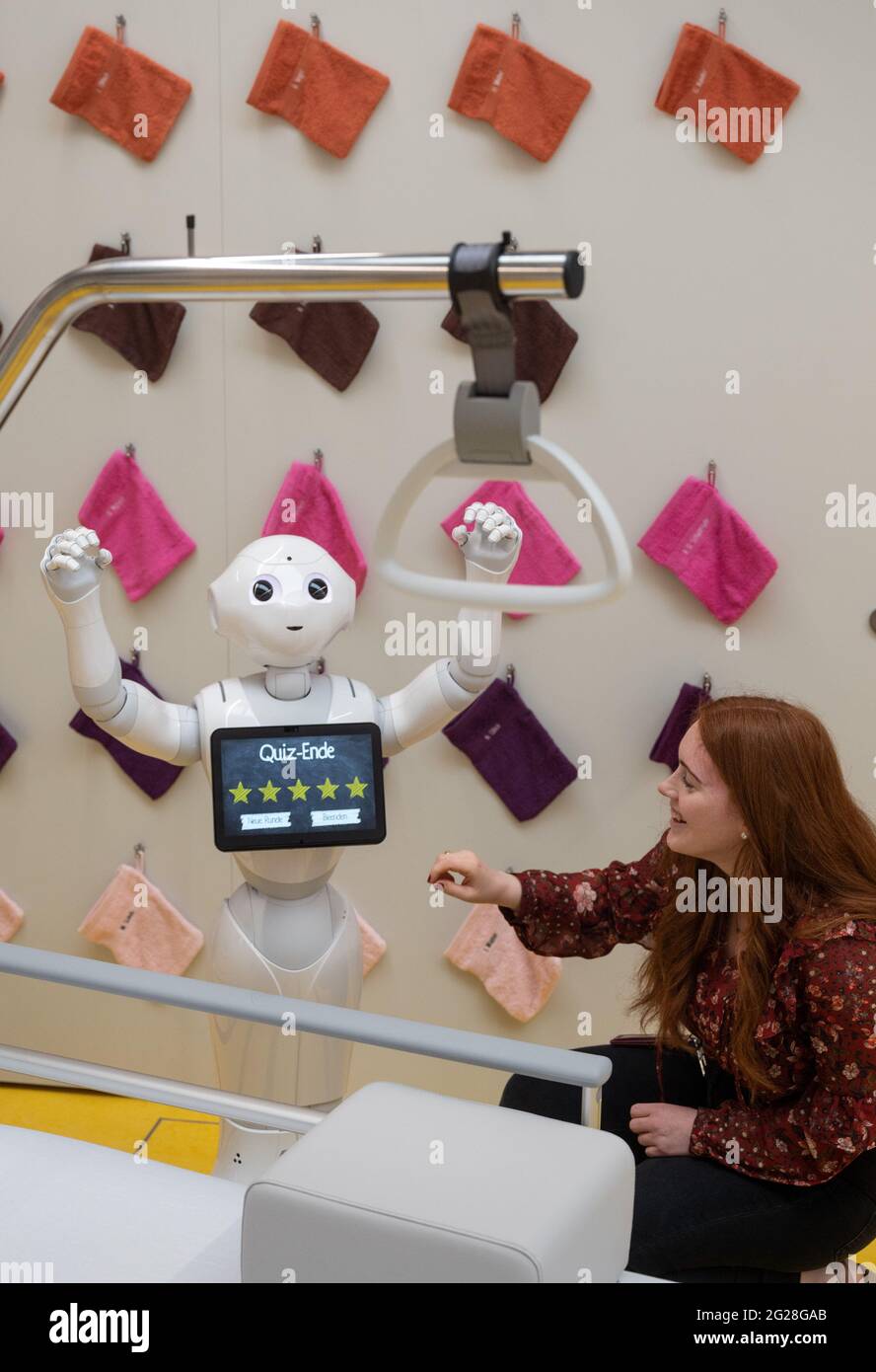 09 June 2021, North Rhine-Westphalia, Dortmund: Magdalena Höbel, volunteer, jokes in the exhibition 'Healing and Caring. Working World in Healthcare' with nursing robot 'Pepper', who shows a jubilant pose after passing a quiz. The robot is able to encourage nursing patients to communicate by taking quizzes, among other things. The show will be on permanent display at the German Occupational Safety and Health Exhibition (Dasa) from 10 June. Covering more than 800 square meters, the interactive exhibition is devoted in particular to the skills and competencies required by people in medical profe Stock Photo