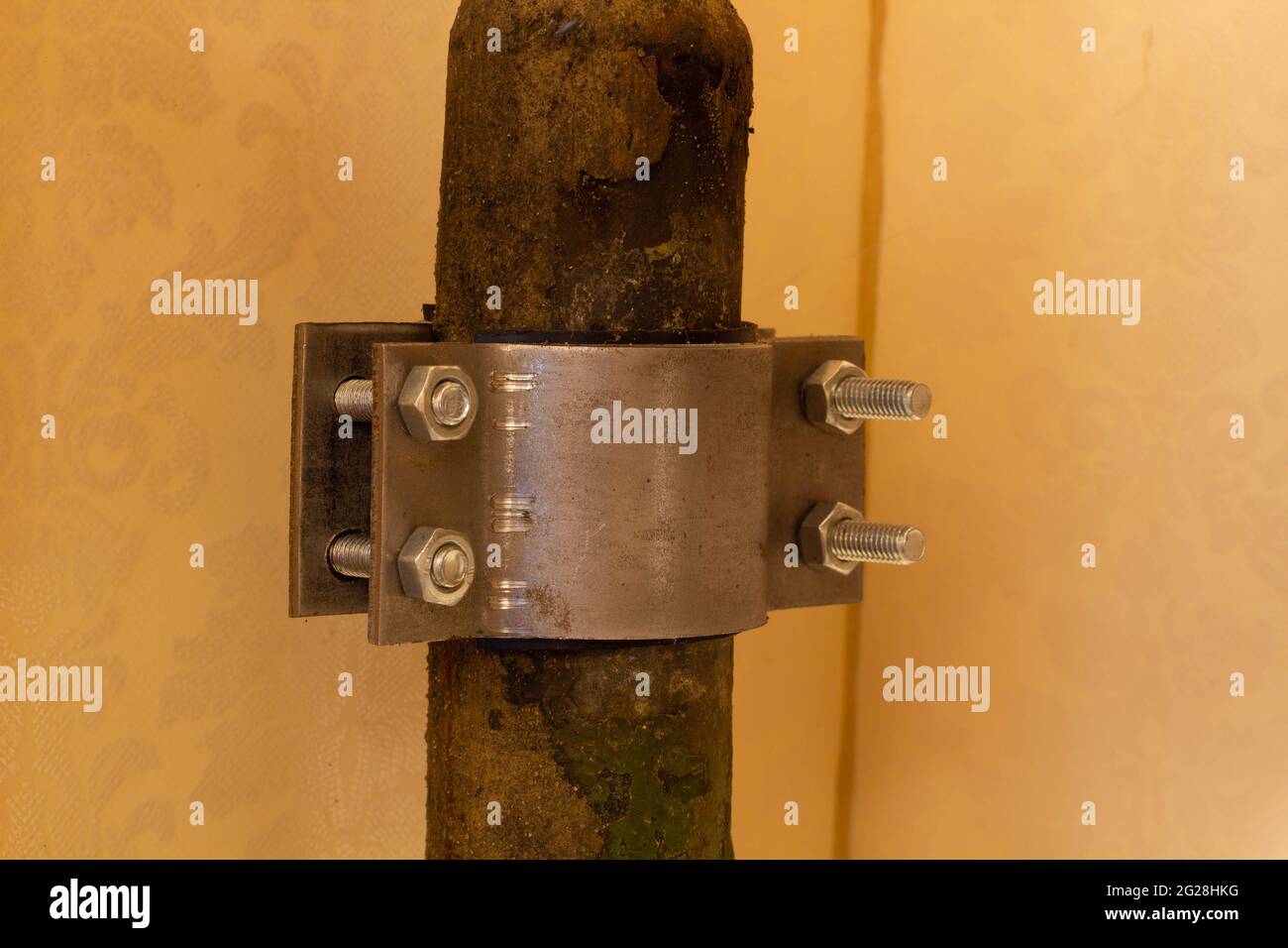 The four-screw M10 stainless steel pipe clamp attached to a rusty metal pipe. Plumbing repair Stock Photo