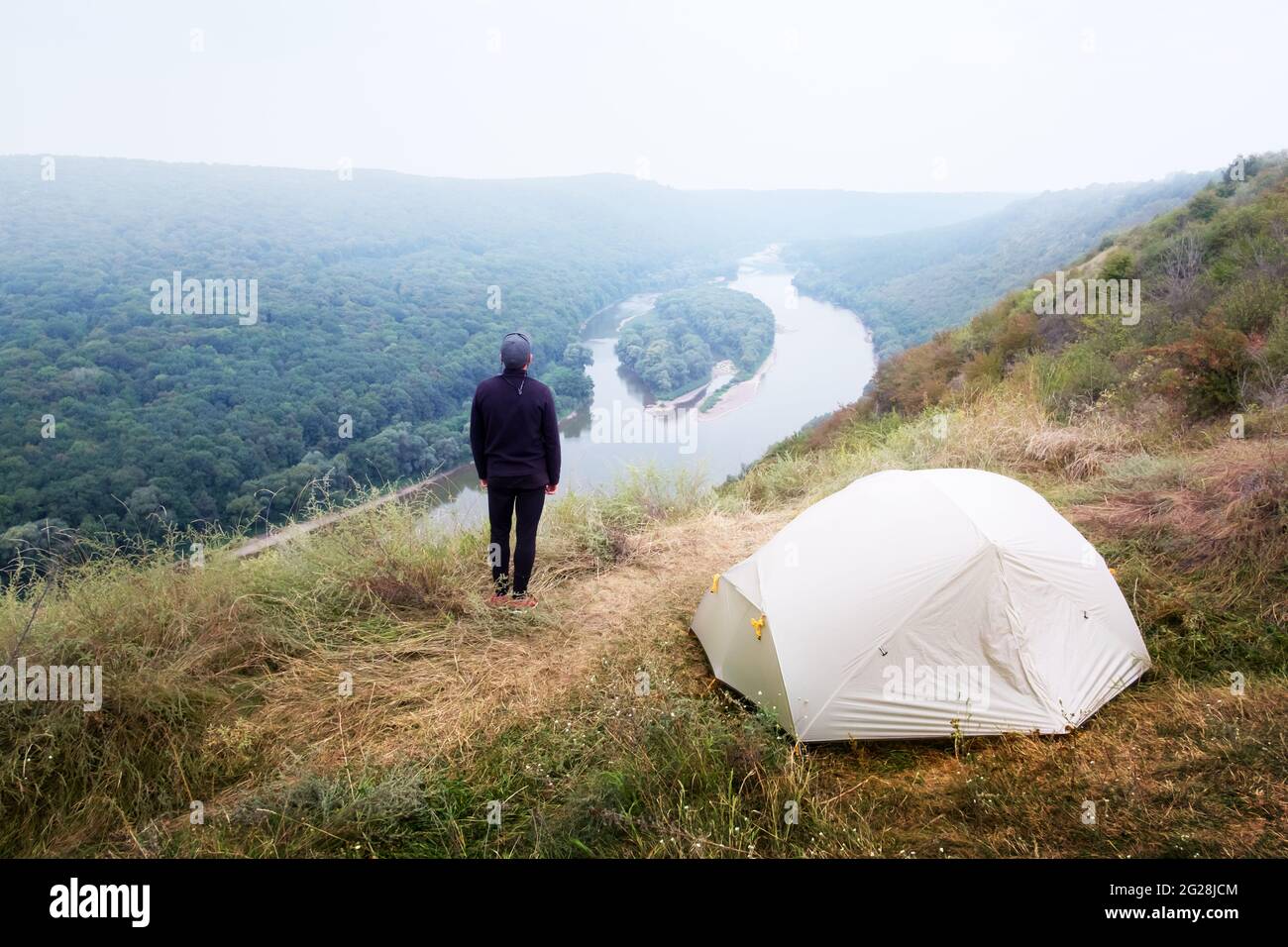 A tourist stands near a tent on the top of a mountain above the majestic Dniester River in Ukraine. Landscape photography Stock Photo
