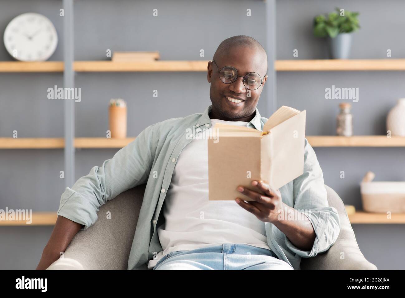 Stay home pastimes. Happy african american mature man enjoying reading book, sitting in comfy armchair, free space Stock Photo