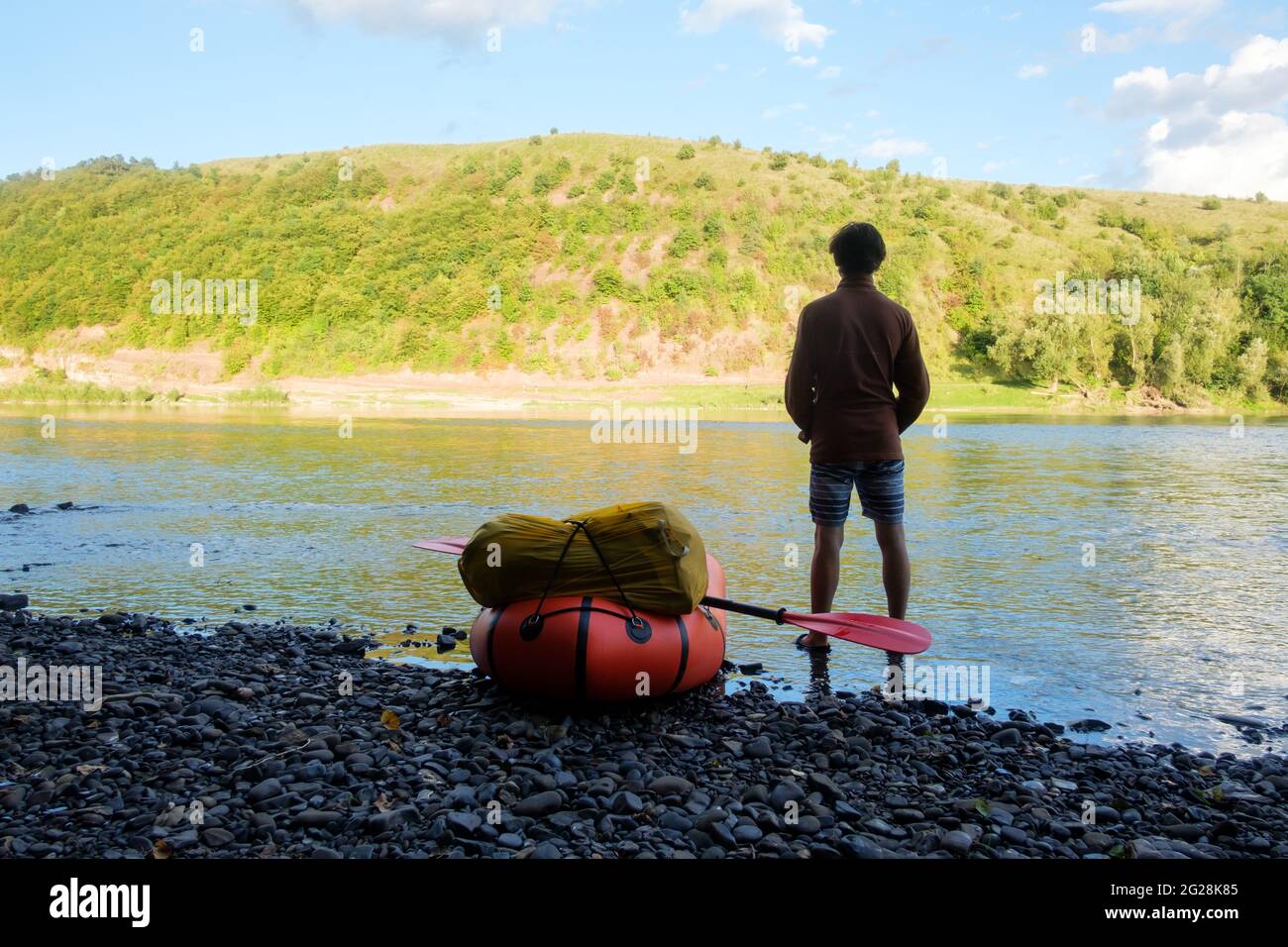 Tourist near yellow packraft rubber boat ready for adventures with red padle on a sunrise river. Packrafting. Active lifestile concept Stock Photo