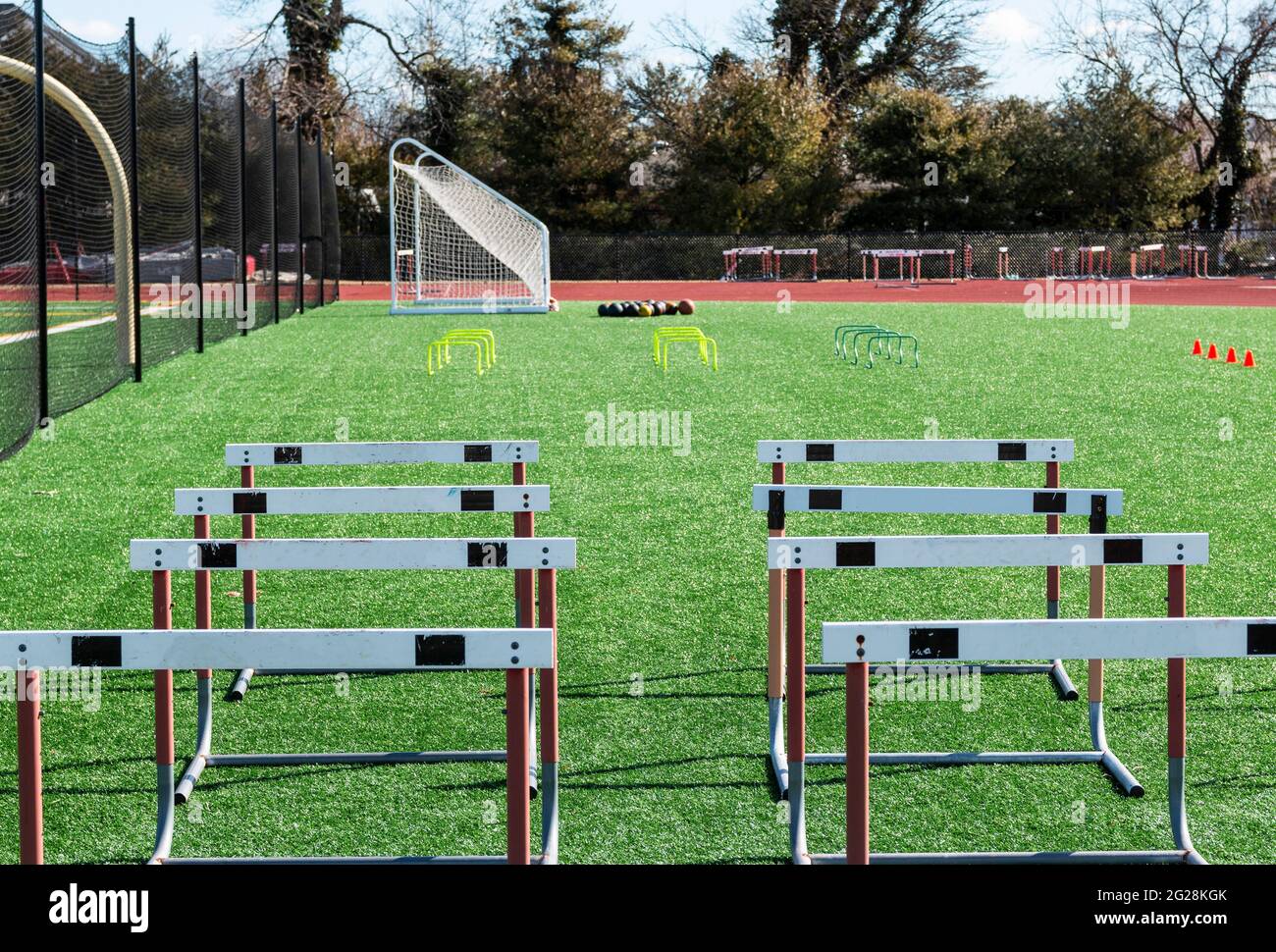 Track hurdles, mini hurdles medicine balls and orange cones set up on a green turf field for track and field strength and agility practice. Stock Photo