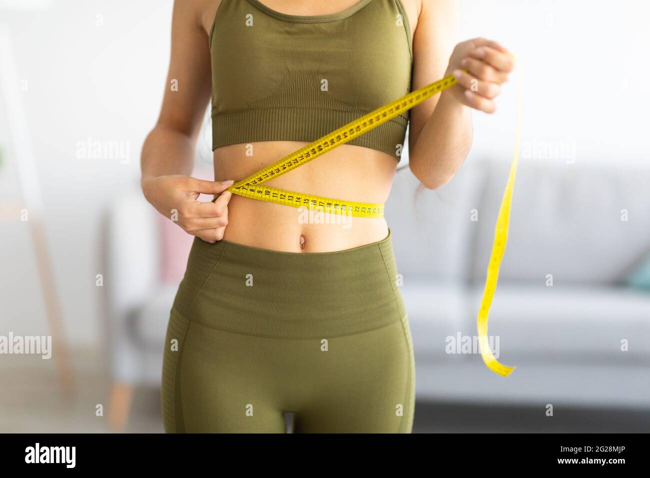 Cropped view of slim Indian woman measuring her waist with tape measure at home, closeup Stock Photo