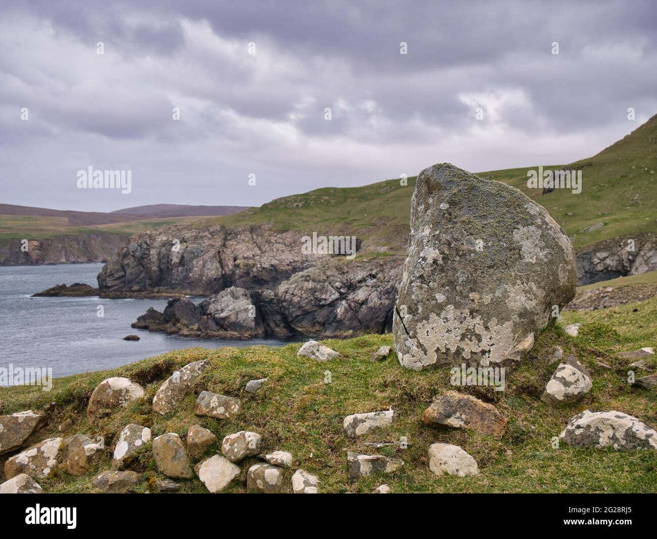 A large boulder and other smaller rocks on the rugged, remote coastline on the Ness of Hillswick, on Mainland, Shetland, UK. Taken on a grey, overcast Stock Photo
