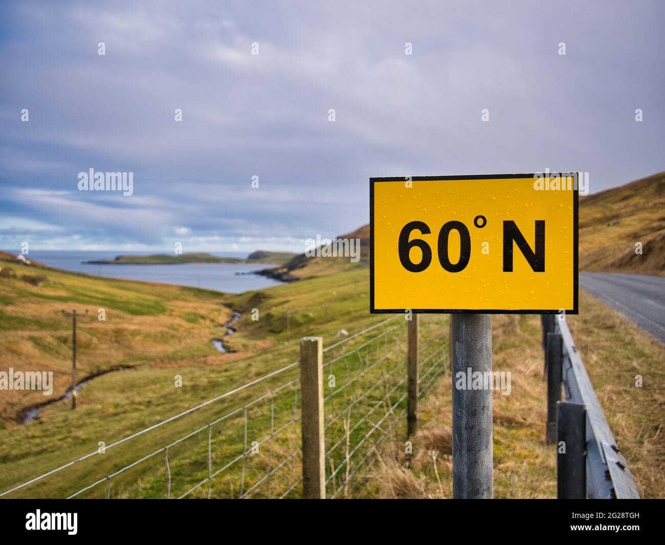 A rectangular, yellow sign with black figures on the A970 on Mainland, Shetland, UK marks the 60 degree North line of latitude. Stock Photo