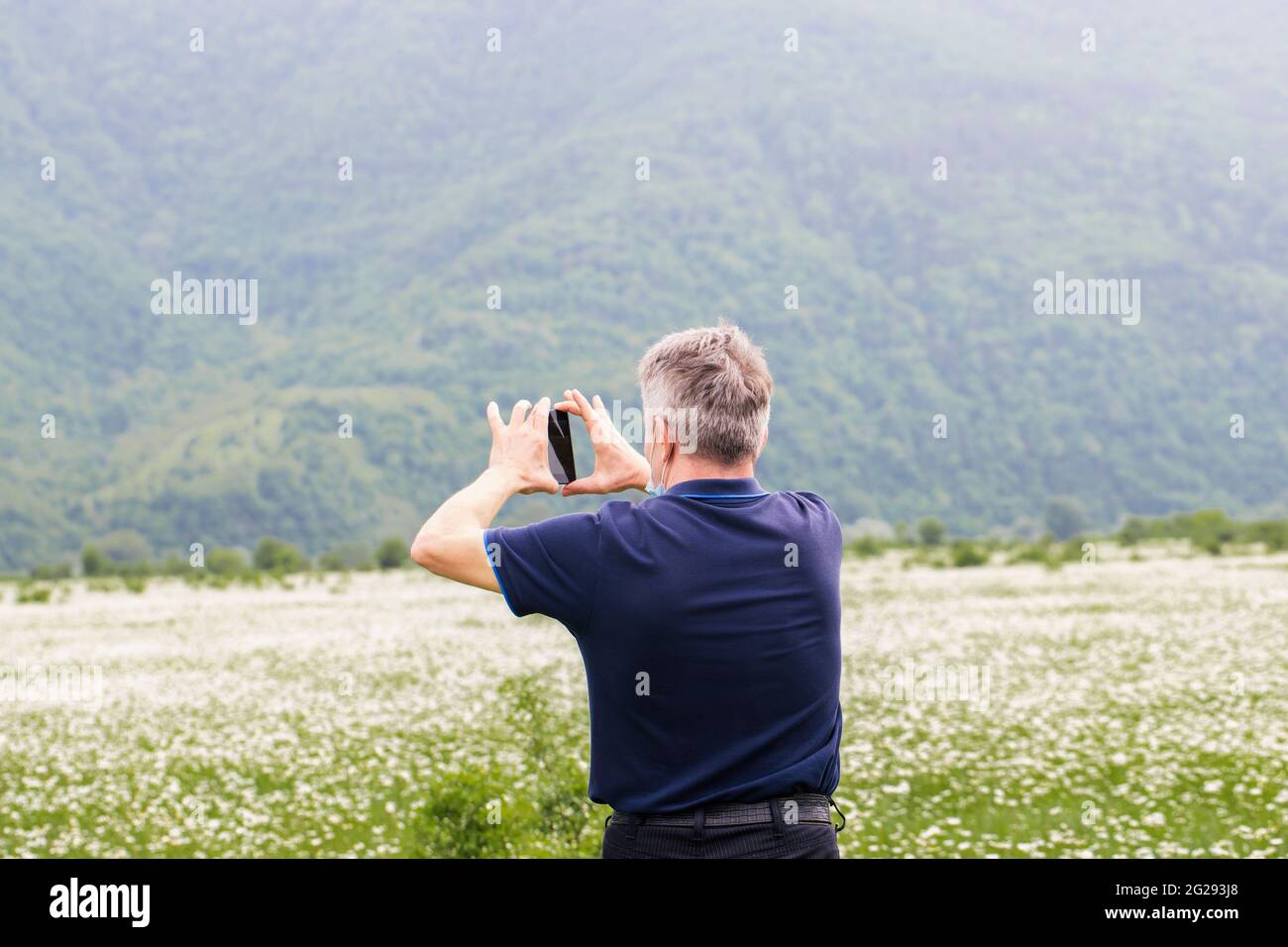 Caucasian man takes a white field of wildflowers daisies on the phone. Chamomiles on the background of mountains. Stock Photo