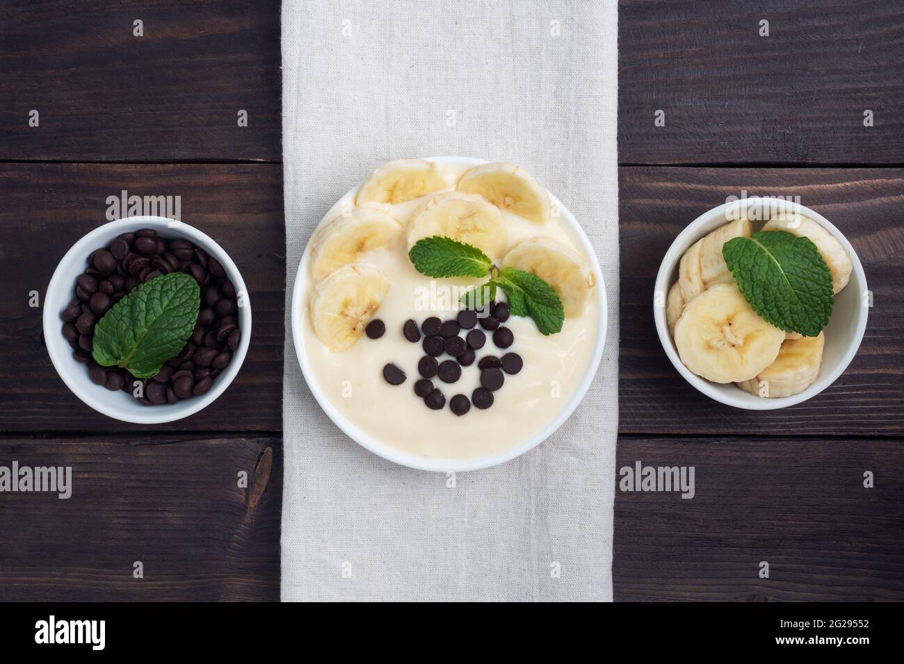 Healthy breakfast, dessert with milk yogurt banana and chocolate on a plate. Dark wooden background Top view Stock Photo