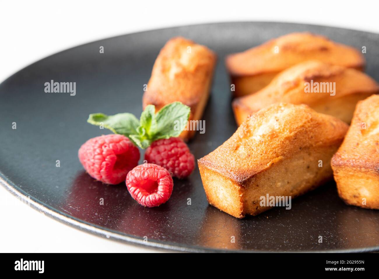 Financier cake - traditional French food on a large, beautiful black plate with raspberries and a mint leaf - a festive concept for Christmas, close-u Stock Photo