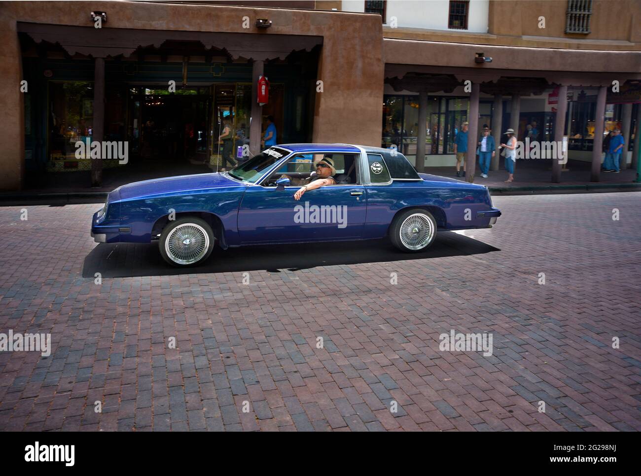 An hispanic man with a customized low-rider car cruises through the historic Plaza in Santa Fe, New Mexico. Stock Photo
