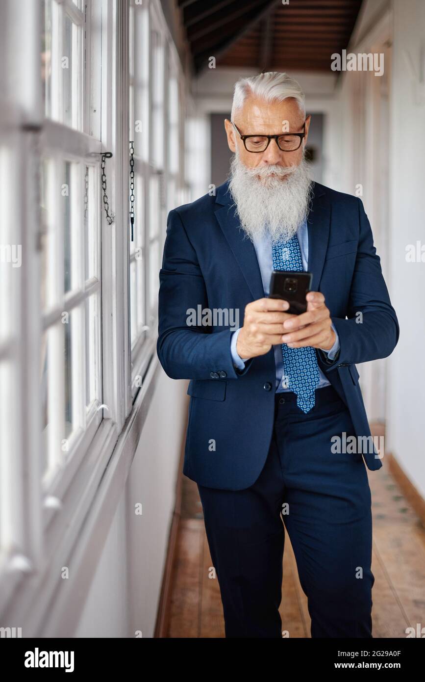 Stylish senior businessman chatting on smartphone in corridor Stock Photo
