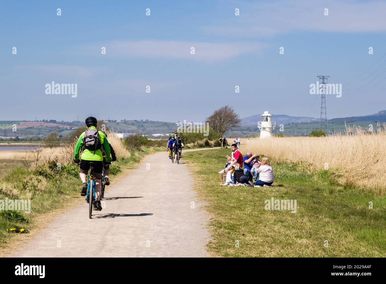 Cyclists cycling on Coastal Path along Severn estuary by East Usk Lighthouse at Newport Wetlands National Nature Reserve. Nash Newport Gwent Wales UK Stock Photo