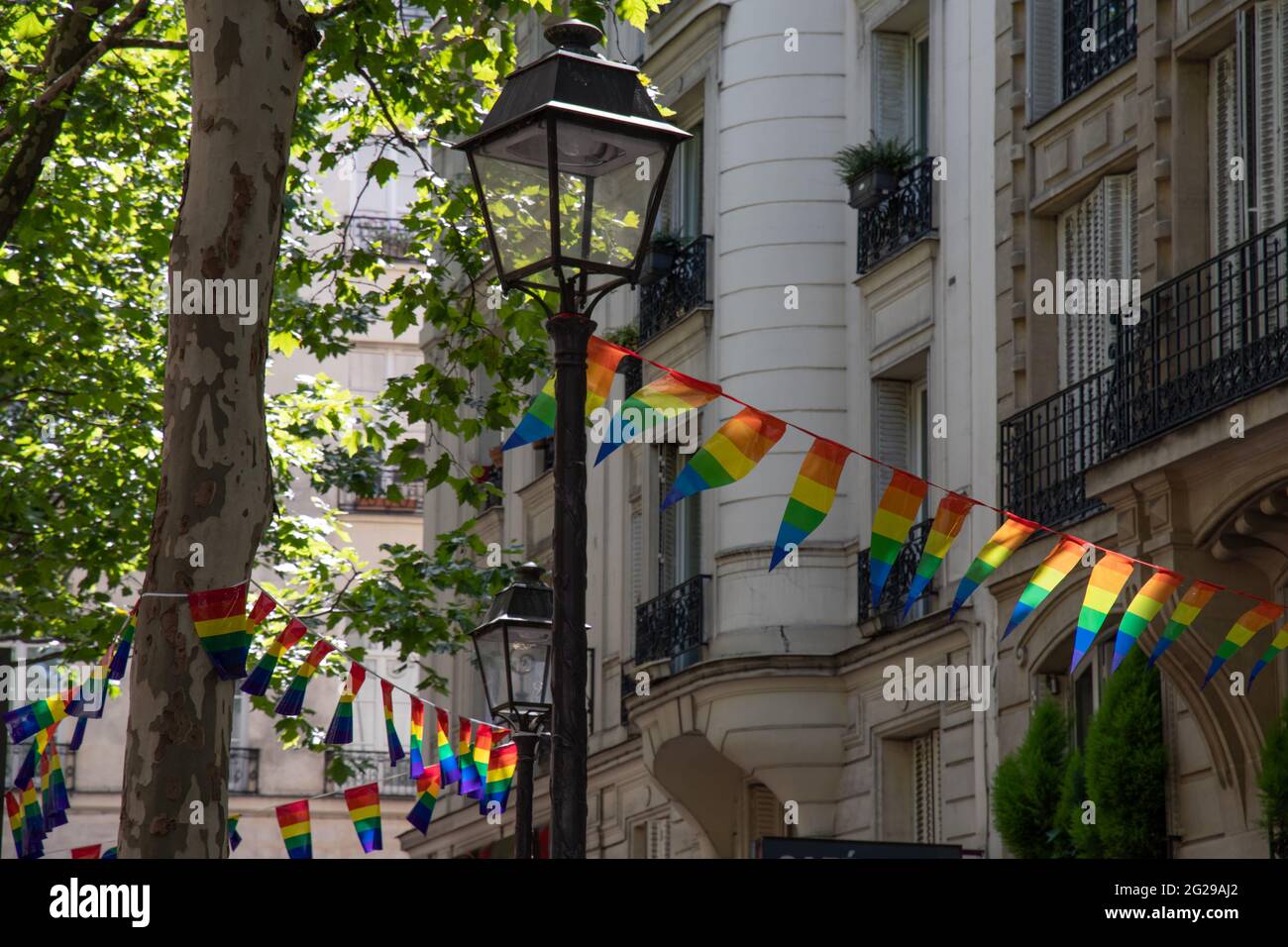 Decoration of triangle shape banners in colors of Lgbtq flags hanging between vintage lantern streetlights and ornate stone house with balconies. Gay Stock Photo