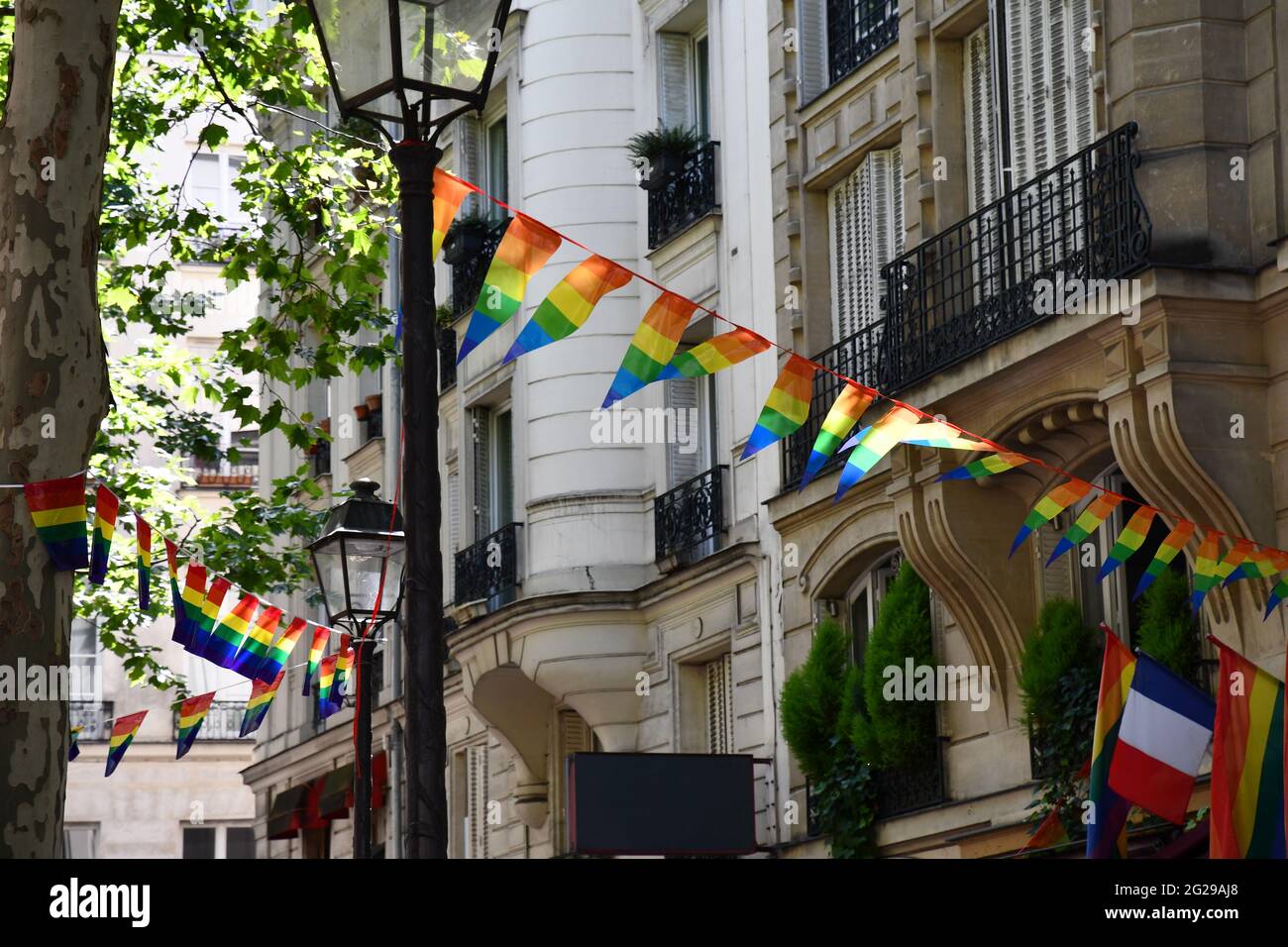 Decoration of triangle shape banners in colors of Lgbtq flags hanging between vintage lantern streetlights and ornate house with balconies. Gay pride Stock Photo